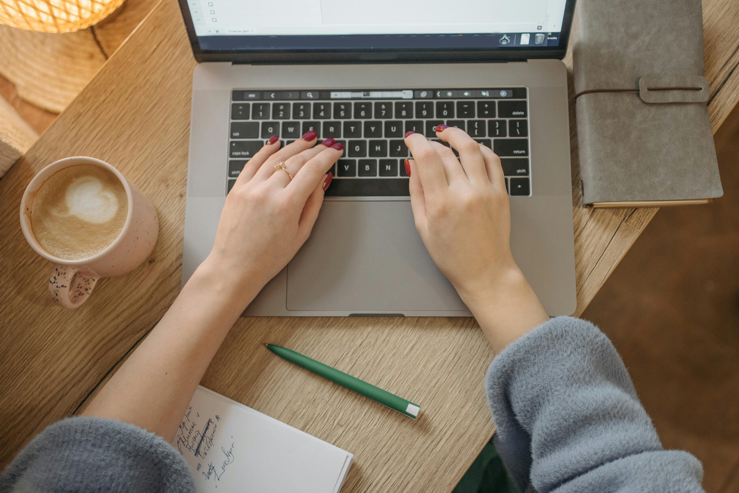 Woman's hands working on the computer with a coffee on the desk.